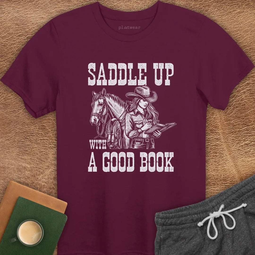 A maroon crew neck t-shirt with a graphic print of a person on a horse and the phrase 'SADDLE UP WITH A GOOD BOOK'.