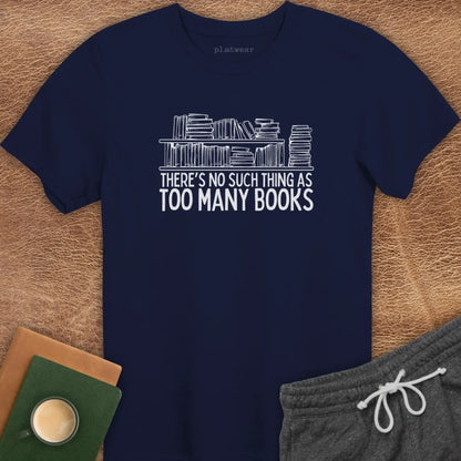 Black crew neck t-shirt with the text 'THERE'S NO SUCH THING AS TOO MANY BOOKS' printed on the front, displayed on a wooden surface alongside a book and a cup of coffee.